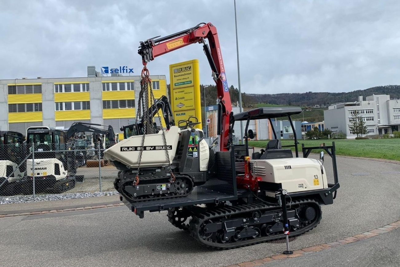 Weisser Raupendumper mit Ladekran und Mini-Dumper am Kran hängend